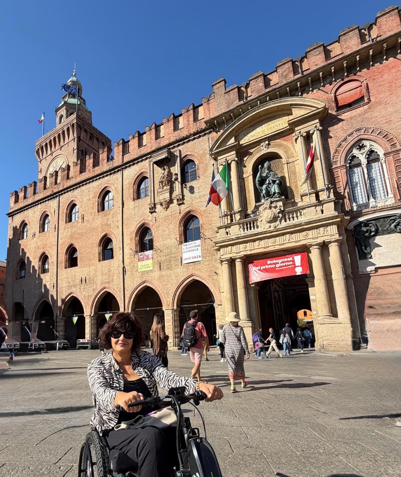 Anna sorridente sul suo Triride in Piazza Maggiore a Bologna, davanti a Palazzo d’Accursio.