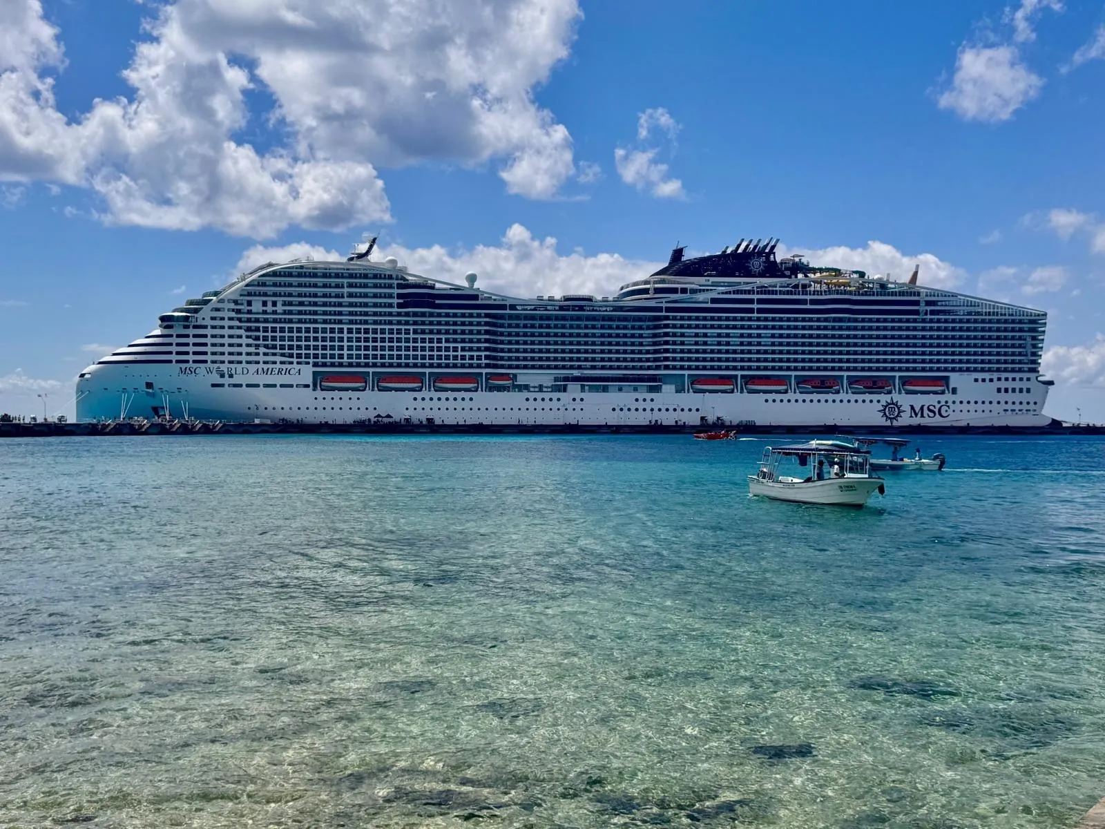 Una grande nave da crociera bianca sul mare turchese dei Caraibi, sotto un cielo con nuvole bianche.